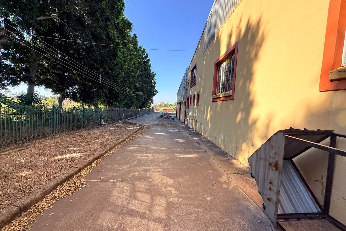 Exterior side view of an industrial property featuring concrete paving, security fencing, and a painted facade with window security bars.