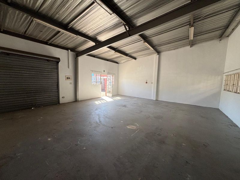 Spacious industrial utility area featuring high exposed ceilings, concrete flooring, and a large roller shutter door for convenient access.