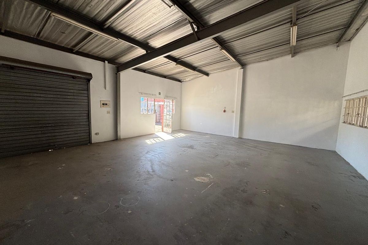 Spacious industrial utility area featuring high exposed ceilings, concrete flooring, and a large roller shutter door for convenient access.