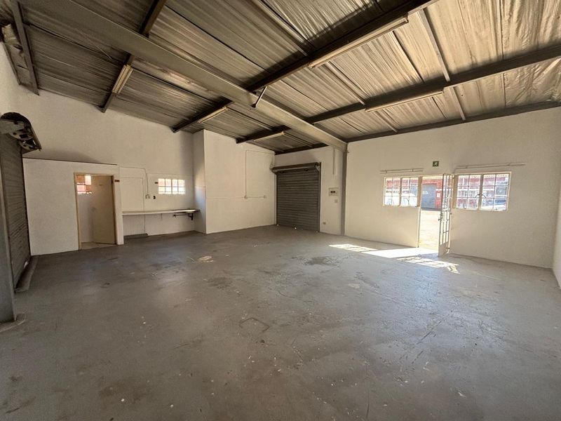 Spacious industrial utility space featuring high exposed ceilings, concrete flooring, and a large roller shutter door, suitable for workshop or storage use.