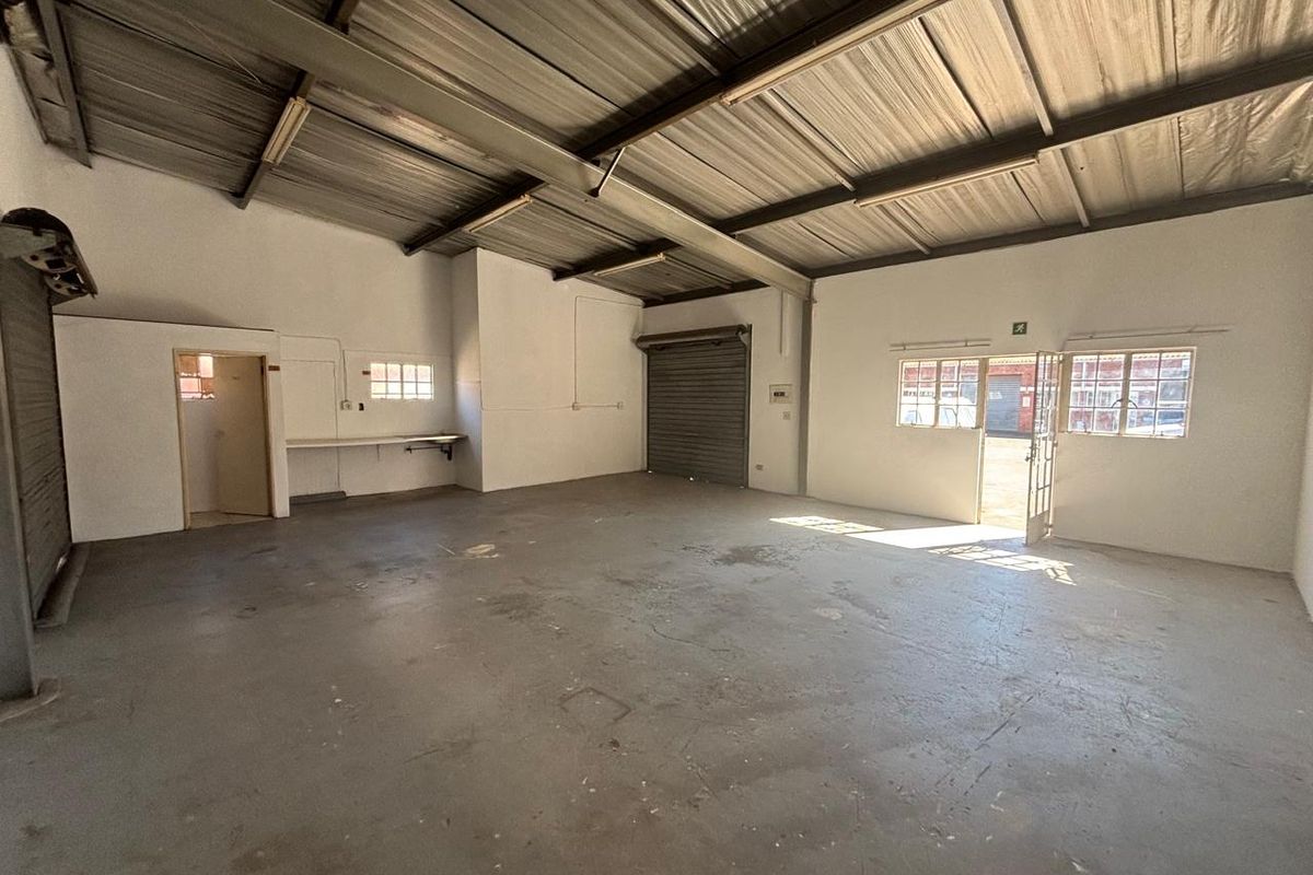 Spacious industrial utility space featuring high exposed ceilings, concrete flooring, and a large roller shutter door, suitable for workshop or storage use.
