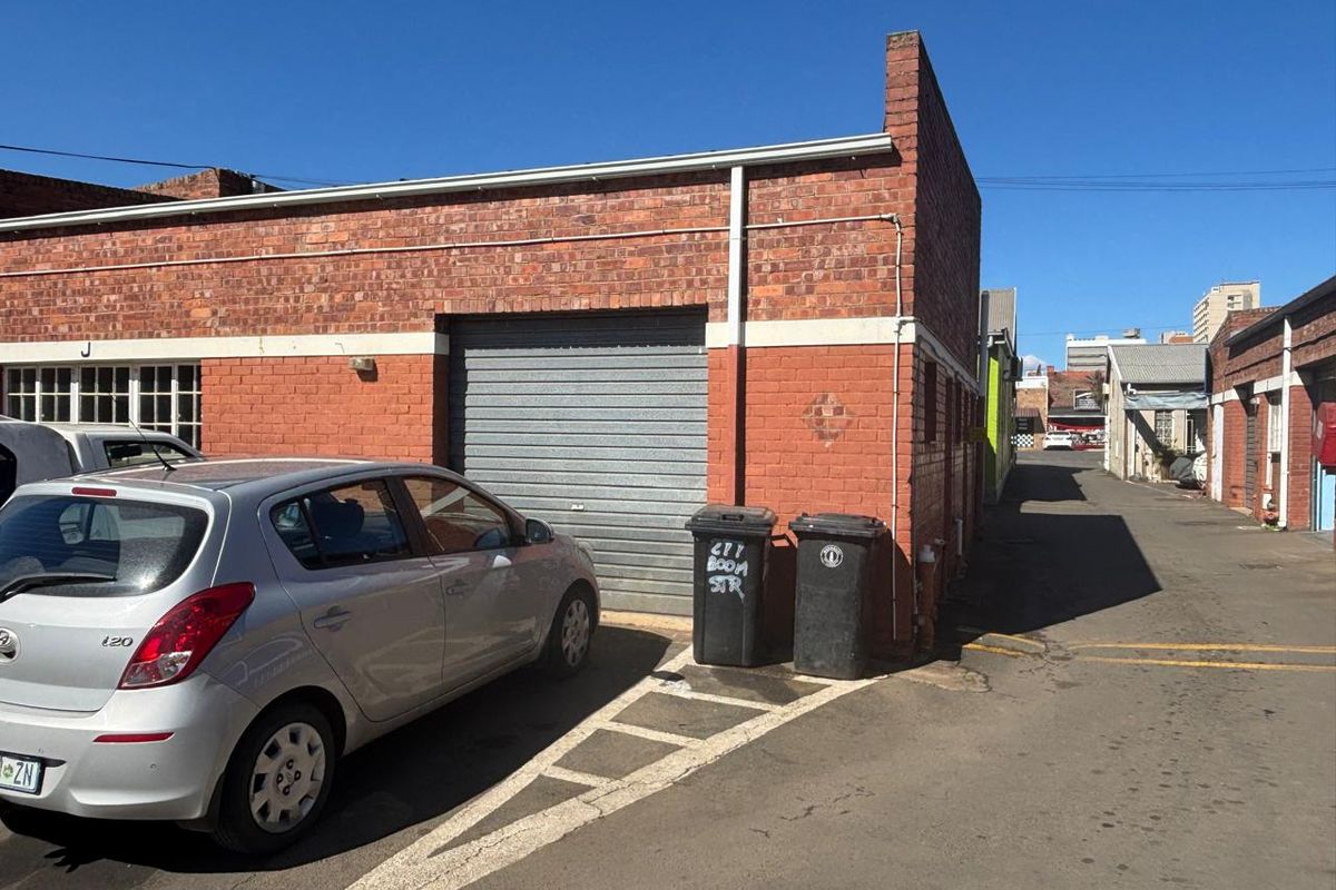 Rear exterior view of an industrial property featuring a roller shutter door and exposed brick facade with adjacent asphalt access lane.