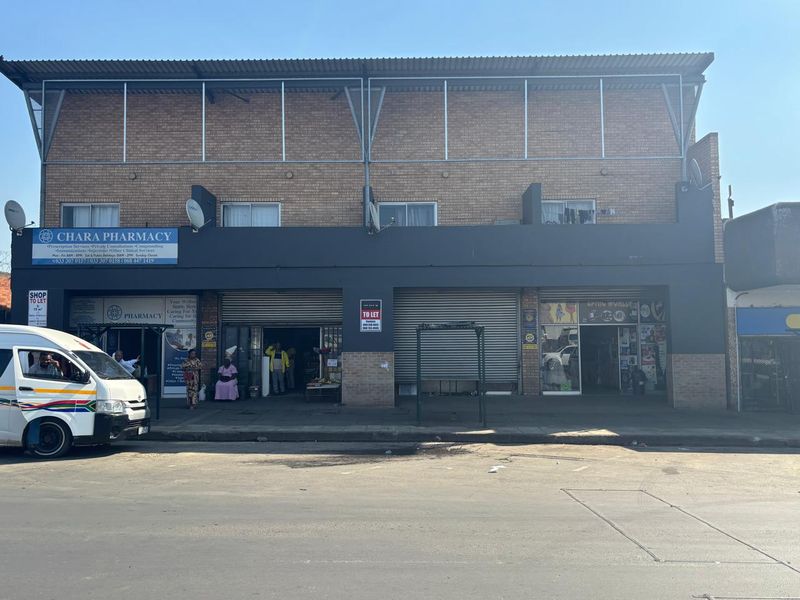 Front elevation of a multi-unit retail property featuring brick construction, metal roller shutters, and commercial signage at street level.