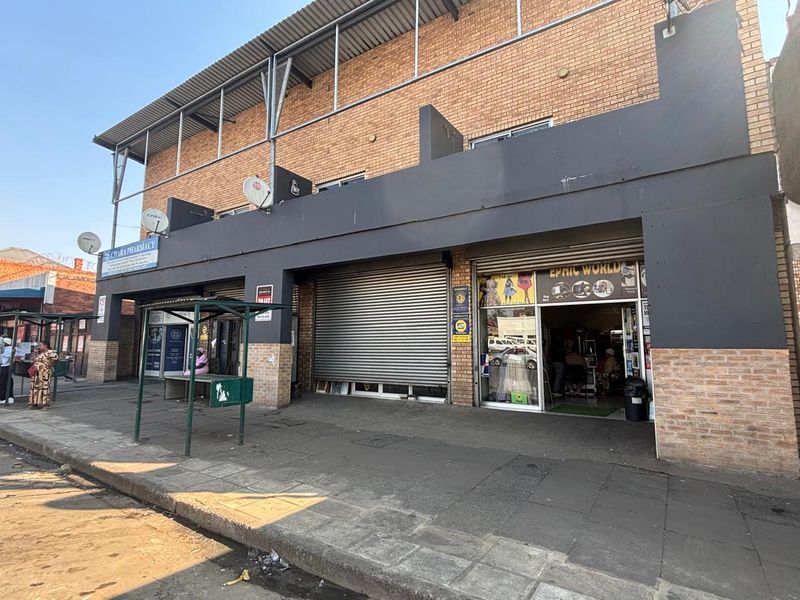 Front elevation of a multi-unit retail property featuring brick facade, metal roller shutter doors, and direct street-level access.