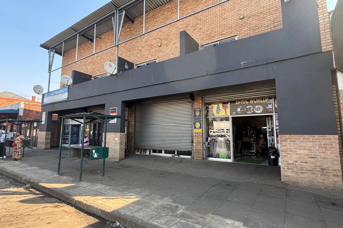 Front elevation of a multi-unit retail property featuring brick facade, metal roller shutter doors, and direct street-level access.