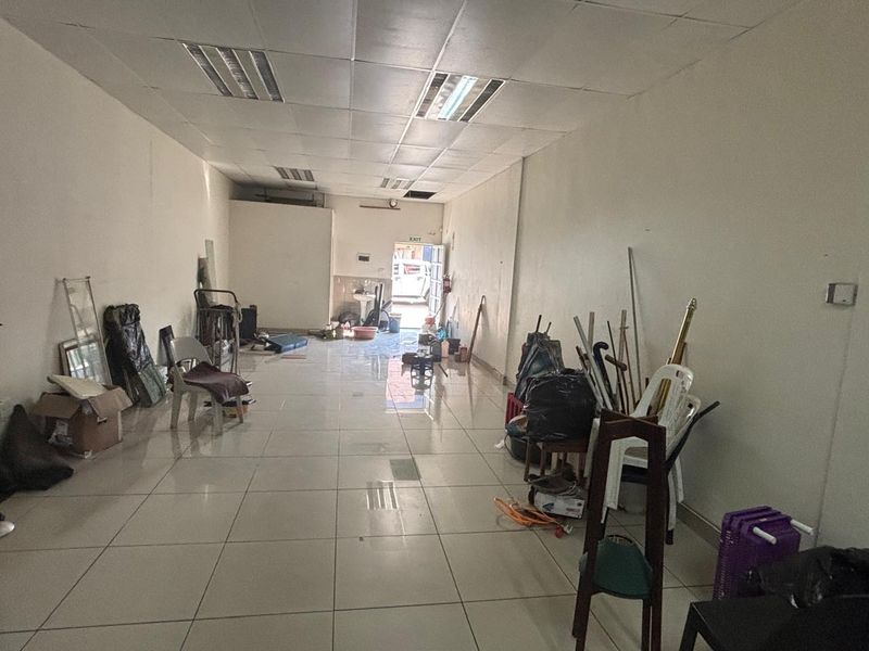 An open-plan retail space featuring tiled flooring and a suspended ceiling with recessed lighting, currently vacant and requiring cosmetic updates.