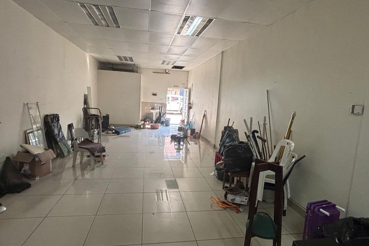 An open-plan retail space featuring tiled flooring and a suspended ceiling with recessed lighting, currently vacant and requiring cosmetic updates.