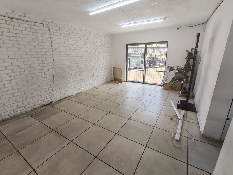 A vacant commercial office space featuring tiled flooring, an exposed brick feature wall, and secure sliding glass door access.