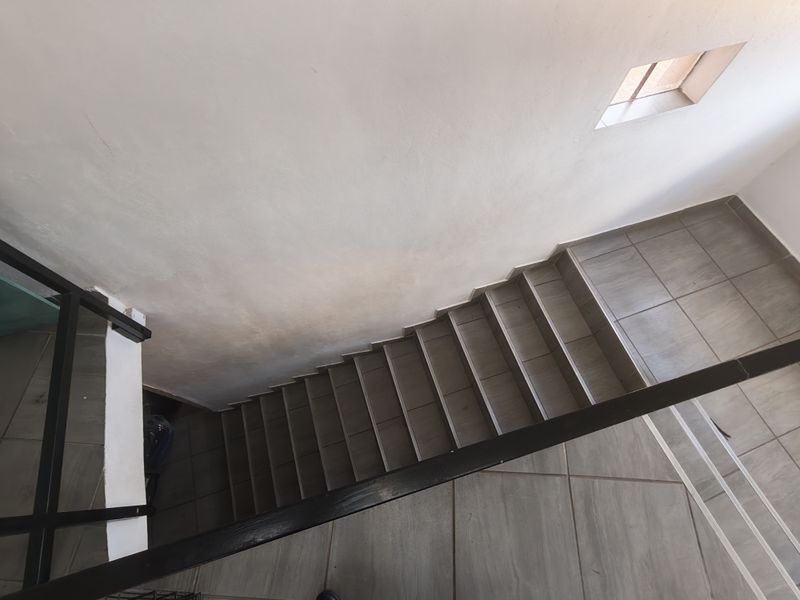A high-angle view of a tiled staircase featuring a black metal handrail and a small window, providing access between building levels.