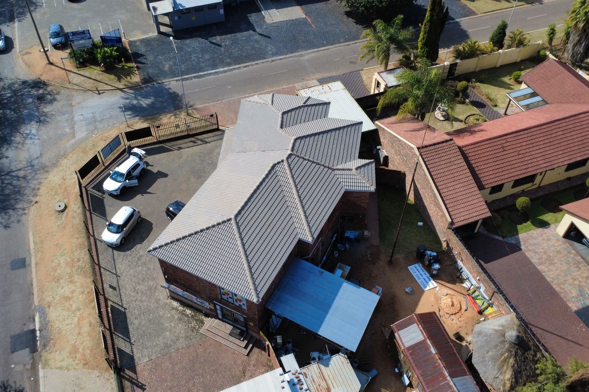Aerial view of the property showing the main building with tiled roofing, paved driveway, perimeter fencing, and surrounding outdoor areas.