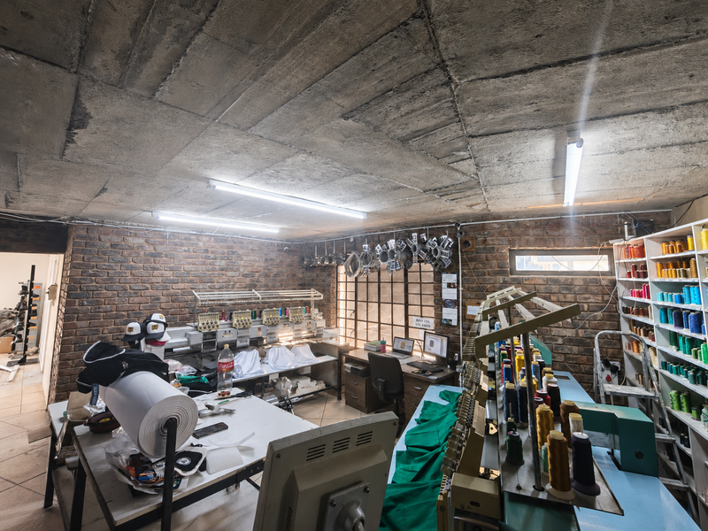 A functional utility workspace featuring exposed brick walls, raw concrete ceiling, fluorescent lighting, and extensive built-in shelving for organized storage.