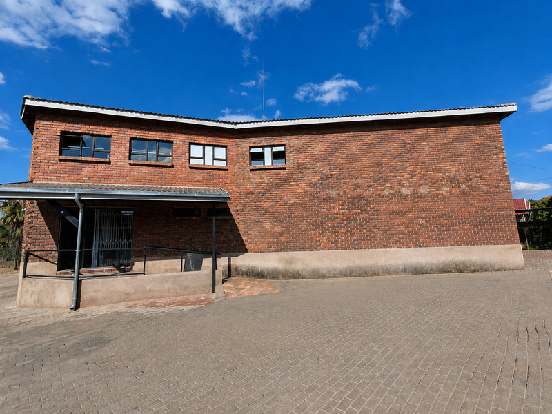 Exterior view of a face brick commercial building featuring a paved driveway, covered entrance with a security gate, and aluminium window frames.