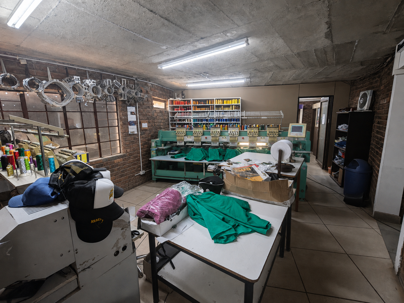 A functional industrial utility space featuring exposed brick walls, tiled flooring, and built-in shelving, currently utilized as an embroidery workshop.