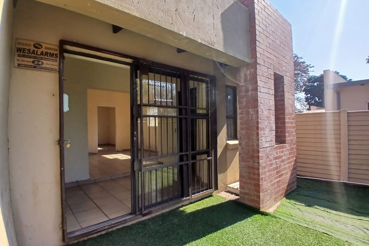 Rear exterior view of the office property featuring a sliding security gate, exposed brick architectural detail, and a small artificial grass area.