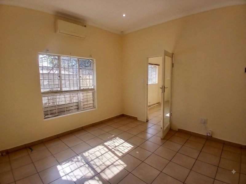 An empty office space featuring tiled flooring, a wall-mounted air conditioning unit, and security bars on the windows.