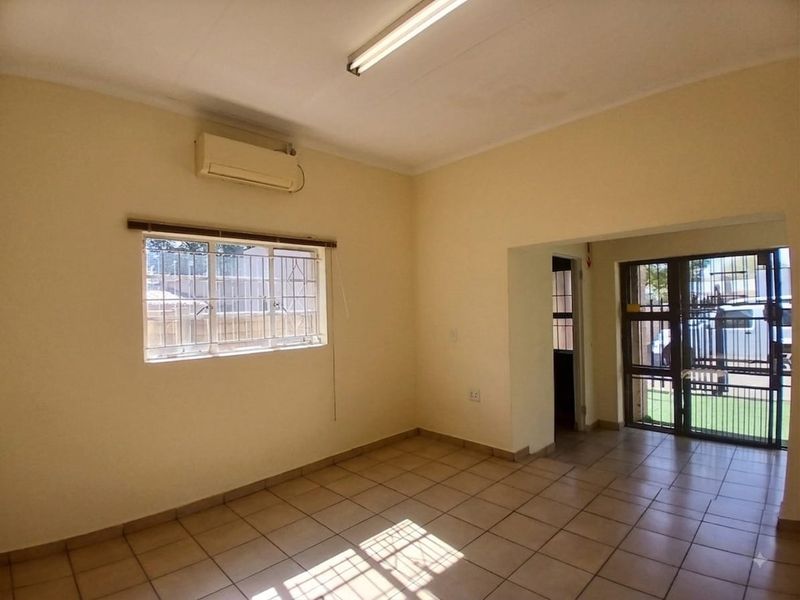 An empty office space featuring tiled flooring, an air conditioning unit, security bars on windows, and a secure entrance gate.