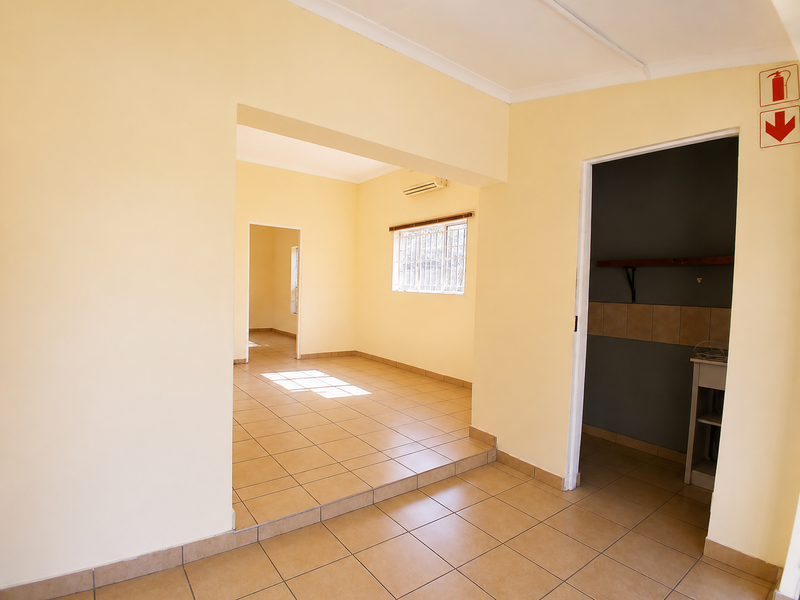 An empty, well-lit office space featuring tiled flooring, an air conditioning unit, and a separate utility or storage area.
