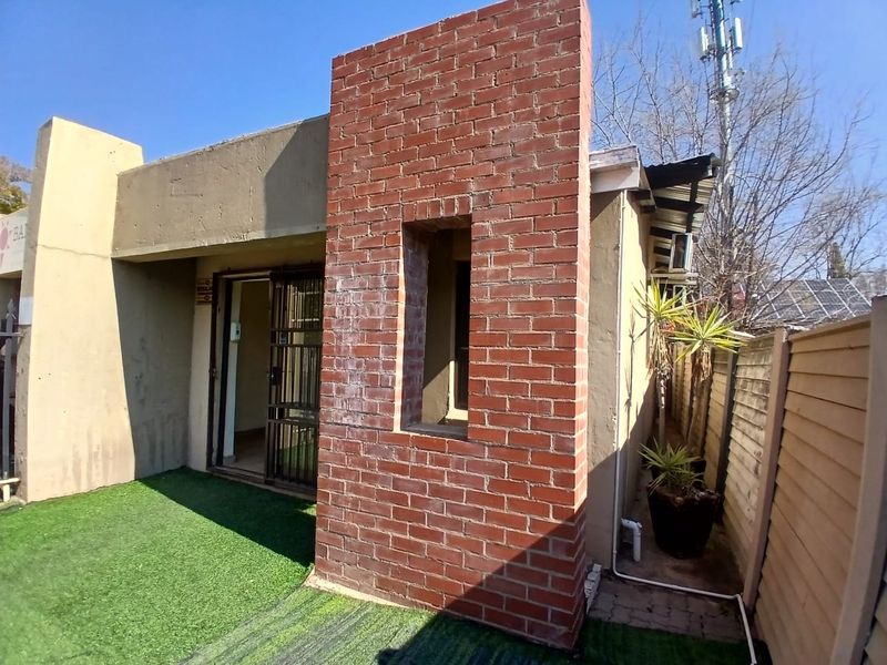 Rear exterior view of the office building featuring an exposed brick architectural element, security gate access, and a low-maintenance artificial grass area.