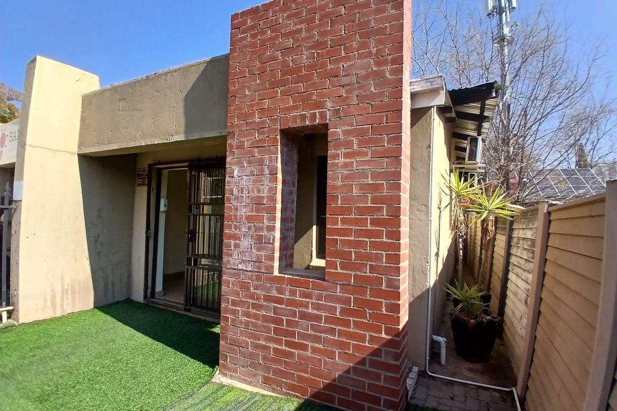 Rear exterior view of the office building featuring an exposed brick architectural element, security gate access, and a low-maintenance artificial grass area.