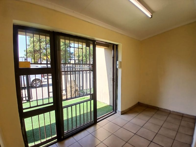 An empty office space featuring tiled flooring, a sliding glass door with security bars, and a fluorescent light fixture.