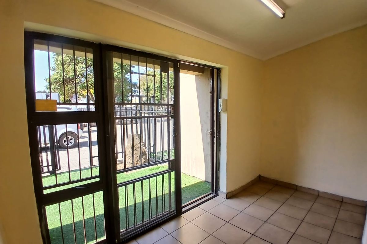An empty office space featuring tiled flooring, a sliding glass door with security bars, and a fluorescent light fixture.