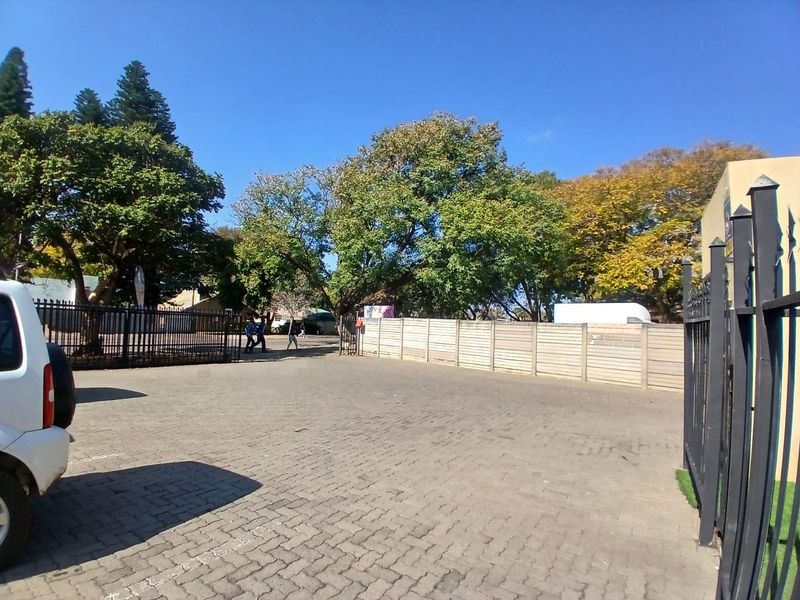 A paved exterior parking area featuring secure metal fencing and perimeter walling, surrounded by mature trees.