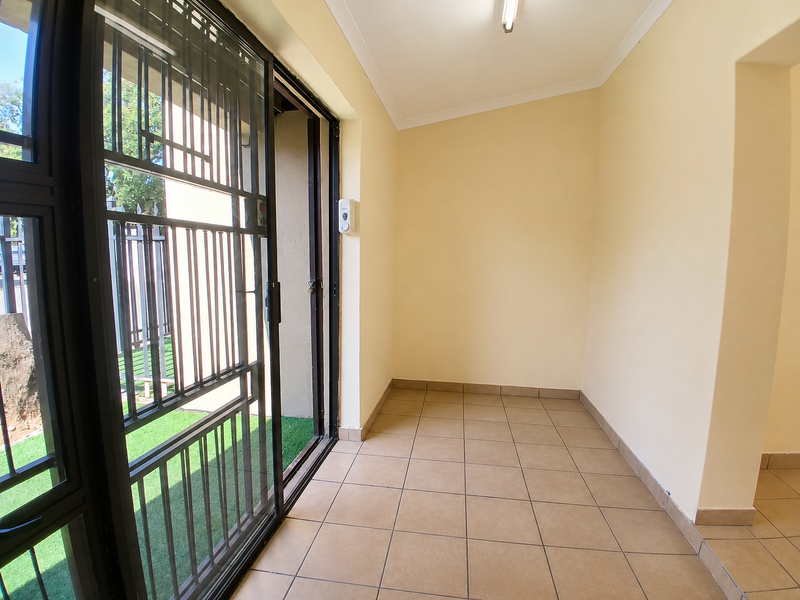 A clean, tiled patio area featuring a secure sliding gate and neutral wall finishes, providing a functional transition space to the outdoors.