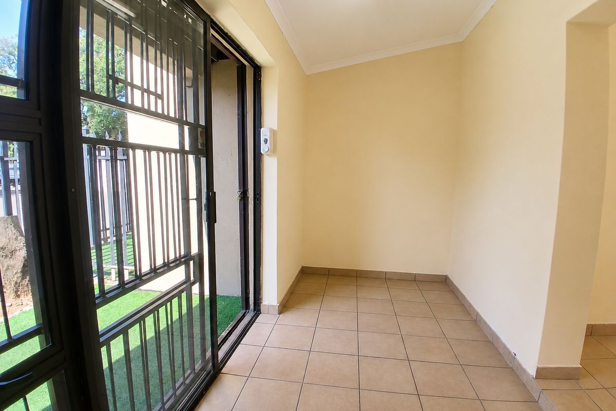 A clean, tiled patio area featuring a secure sliding gate and neutral wall finishes, providing a functional transition space to the outdoors.