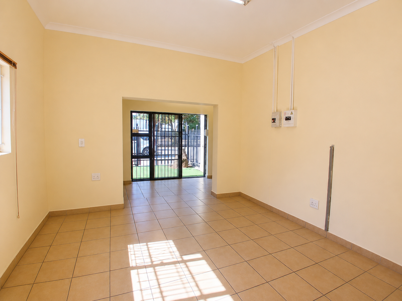 A clean, empty office space featuring neutral walls, ceramic tiled flooring, and a secure entrance gate leading to the exterior.