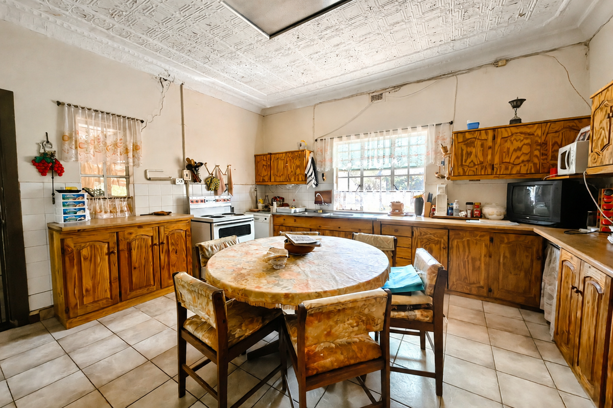 A dated kitchen featuring wooden cabinetry, tiled flooring, and a unique pressed metal ceiling, offering significant potential for a modern renovation.