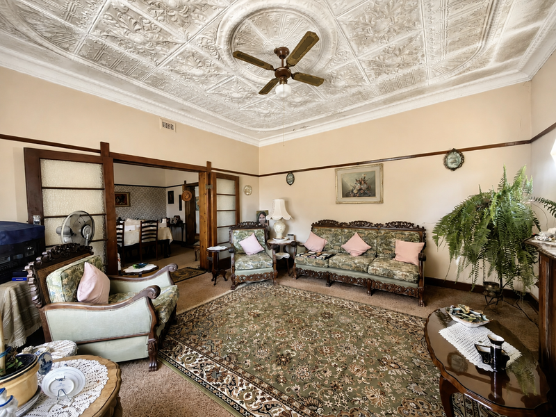 Spacious living room featuring a classic ornate pressed metal ceiling, ceiling fan, and sliding timber room dividers leading to the adjacent dining area.