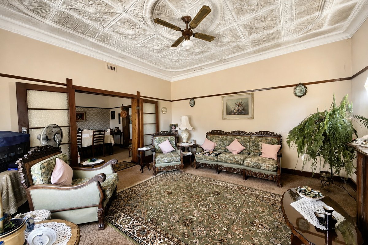 Spacious living room featuring a classic ornate pressed metal ceiling, ceiling fan, and sliding timber room dividers leading to the adjacent dining area.