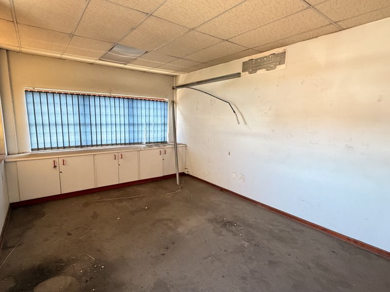 An empty office space featuring built-in cabinetry, security bars on windows, and a suspended ceiling, requiring cosmetic refurbishment and repairs.