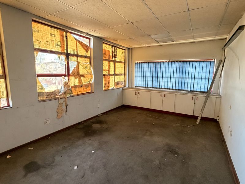 An empty office space featuring built-in cabinetry, carpet flooring, and a suspended ceiling, currently requiring cosmetic refurbishment and repairs.