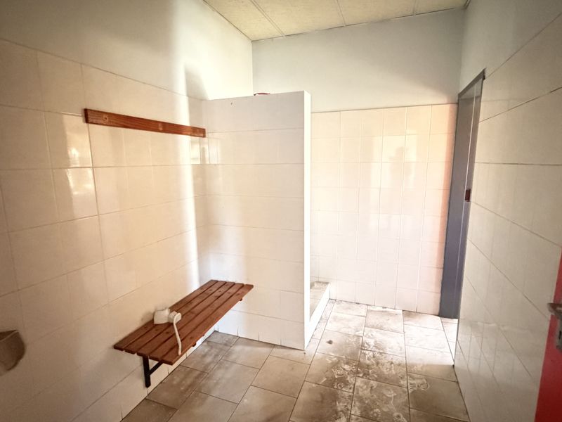 A functional industrial-style bathroom or changing area featuring tiled walls, a built-in shower partition, and a wall-mounted wooden bench.