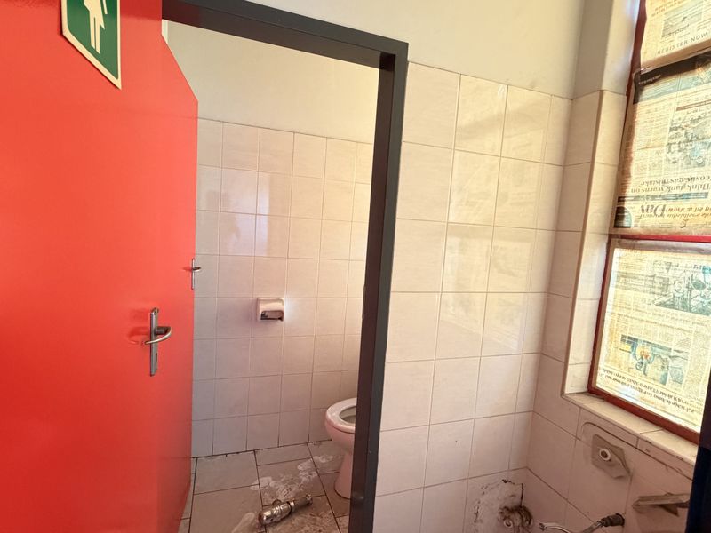 A small industrial bathroom featuring tiled walls and flooring, currently requiring maintenance and the installation of missing plumbing fixtures.