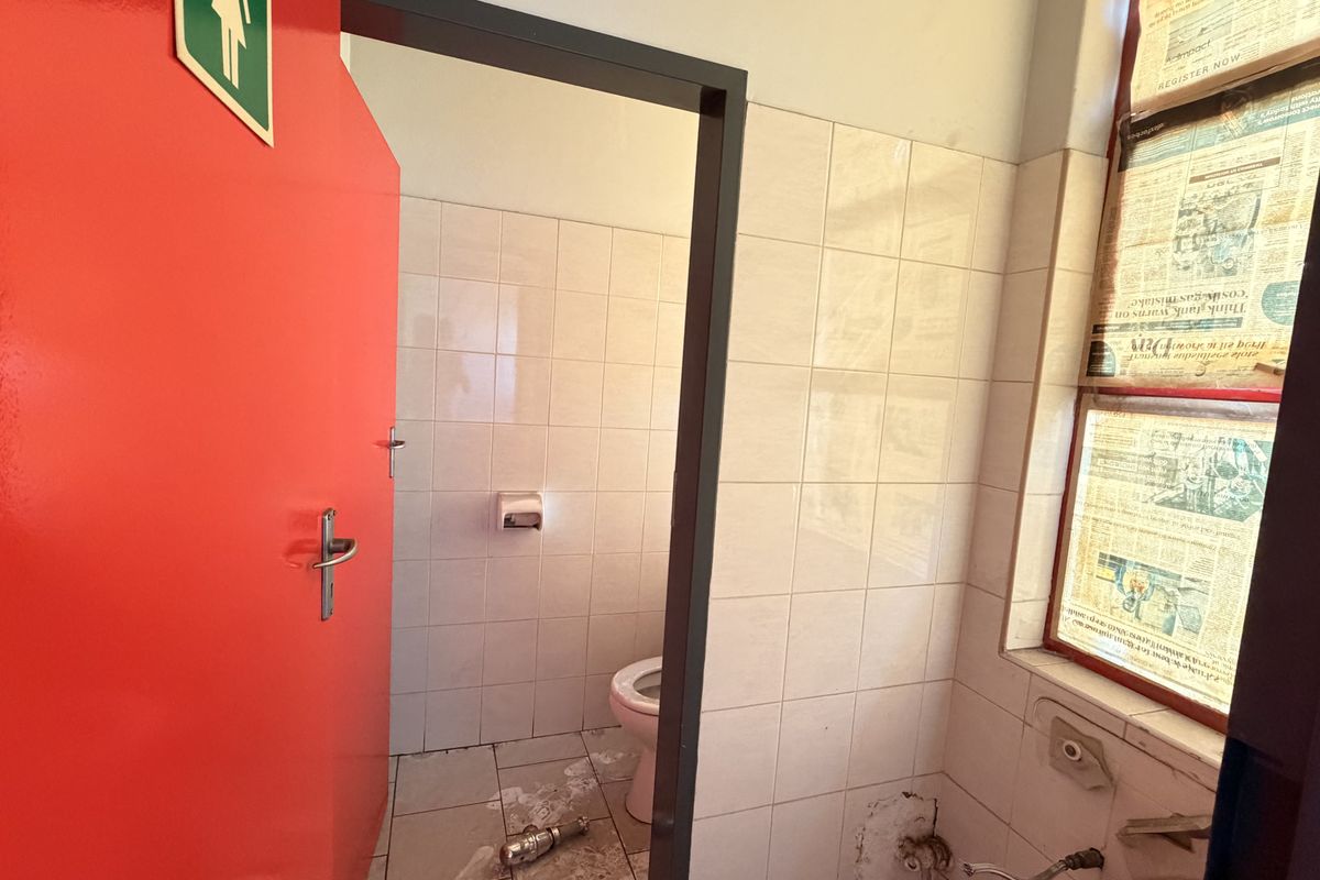 A small industrial bathroom featuring tiled walls and flooring, currently requiring maintenance and the installation of missing plumbing fixtures.