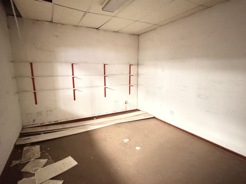 An empty office space featuring a suspended ceiling, wall-mounted shelving brackets, and electrical outlets, currently requiring maintenance and refurbishment.
