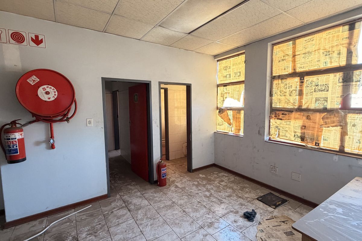 Industrial utility space featuring tiled flooring, suspended ceiling, and essential fire safety equipment, including a hose reel and extinguisher.