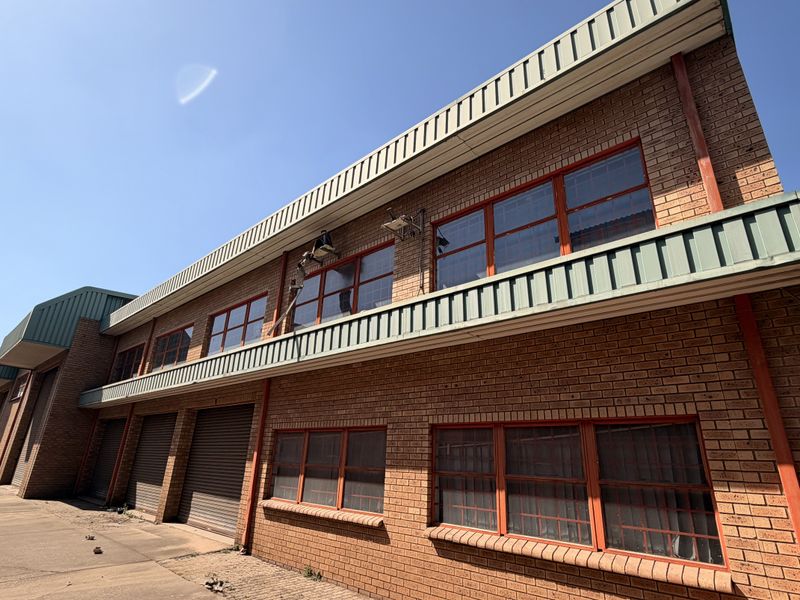 Exterior view of an industrial property featuring a face brick facade, multiple roller shutter doors, and steel-framed windows with security bars.