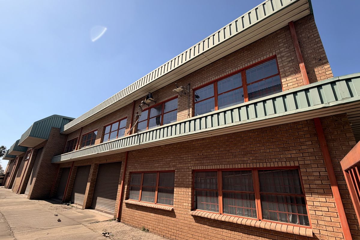 Exterior view of an industrial property featuring a face brick facade, multiple roller shutter doors, and steel-framed windows with security bars.
