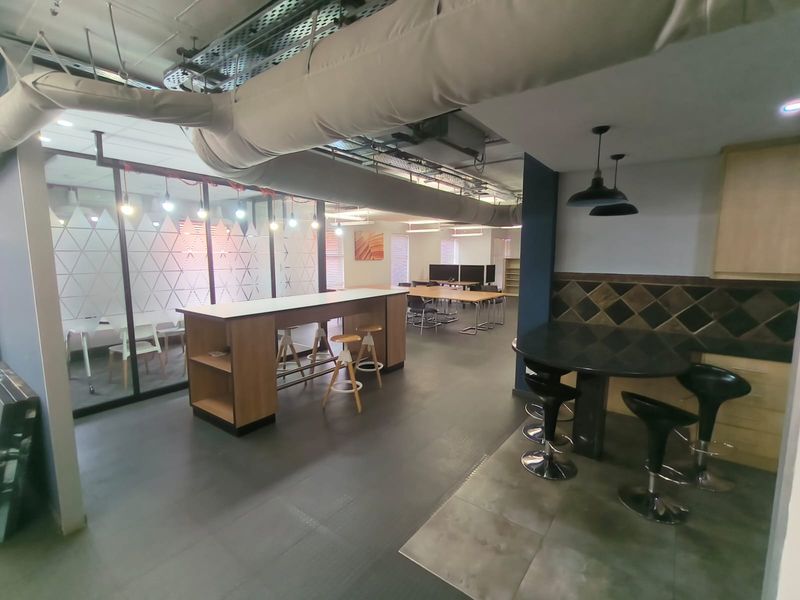 Modern open-plan office space featuring exposed industrial ductwork, glass-partitioned meeting areas, and integrated kitchenette facilities with contemporary finishes.