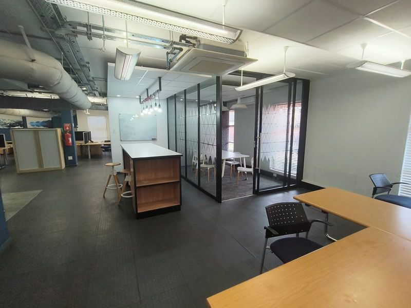 Modern open-plan office space featuring industrial-style exposed ceiling ducting, glass-partitioned meeting rooms, and durable rubber flooring.