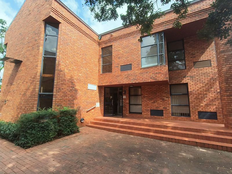 Front exterior view of a professional office building featuring a classic red brick facade, paved entrance area, and large aluminium-framed windows.