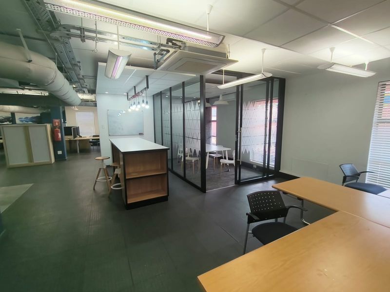 Modern open-plan office space featuring a glass-enclosed meeting room, exposed industrial ceiling services, and durable vinyl flooring.