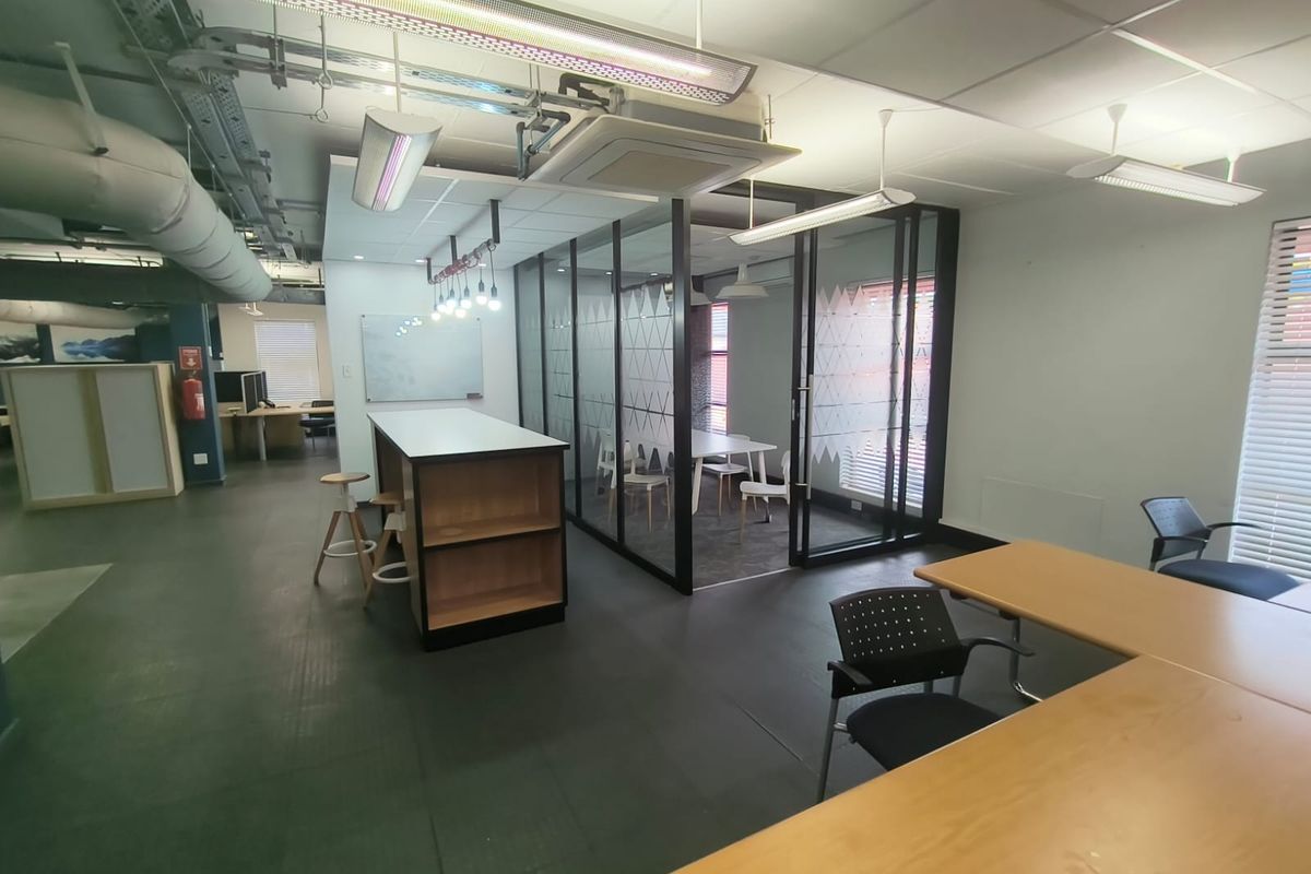 Modern open-plan office space featuring a glass-enclosed meeting room, exposed industrial ceiling services, and durable vinyl flooring.