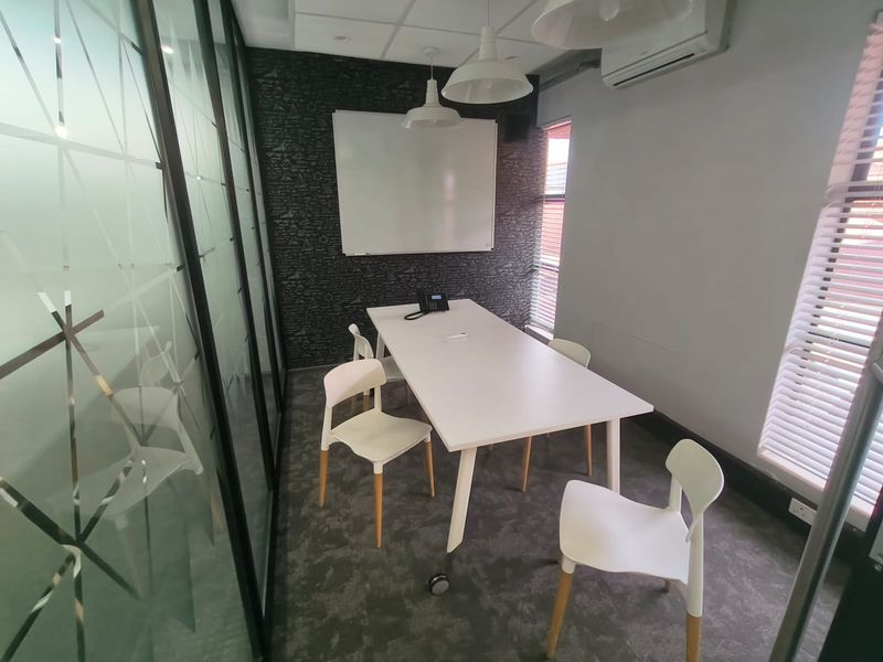 A modern office meeting room featuring a glass partition wall, carpeted flooring, wall-mounted whiteboard, and integrated air conditioning.