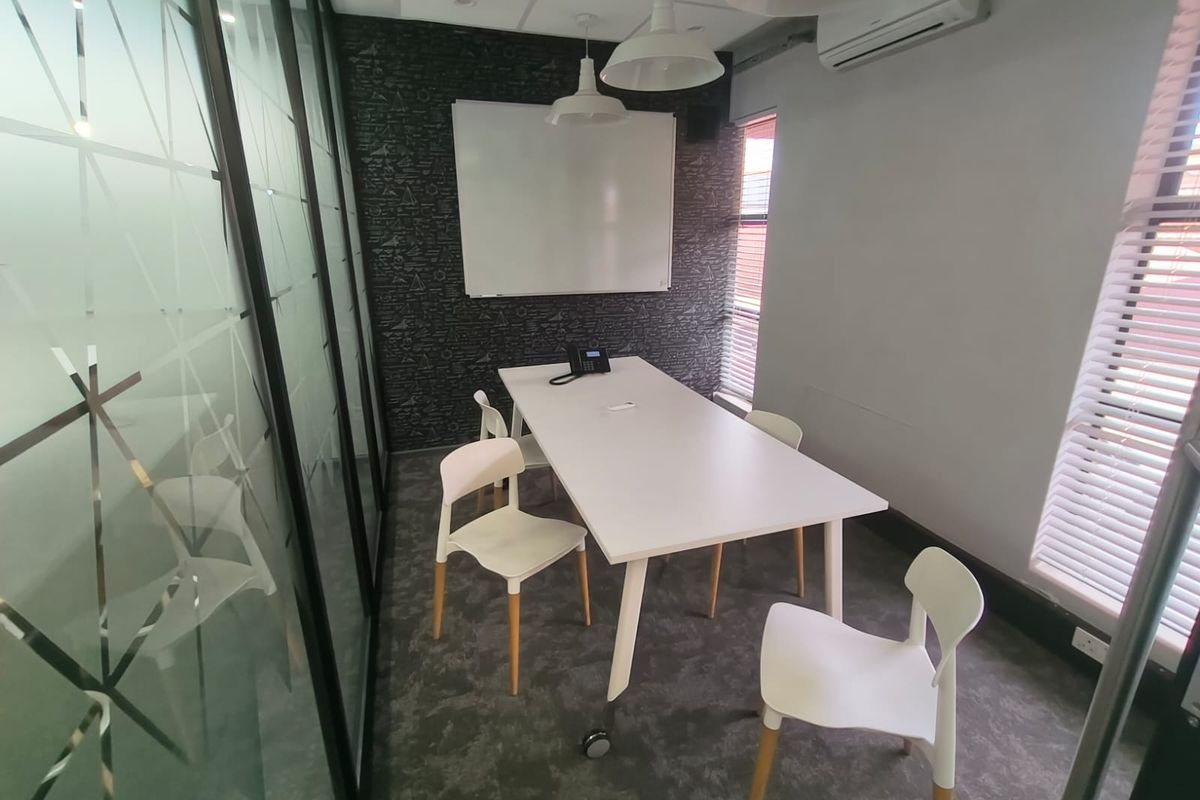 A modern office meeting room featuring a glass partition wall, carpeted flooring, wall-mounted whiteboard, and integrated air conditioning.
