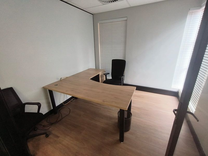 A functional office space featuring laminate flooring, suspended ceiling, and large windows with fitted venetian blinds.