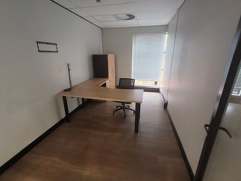 A functional office space featuring laminate flooring, a suspended ceiling with integrated air conditioning, and large windows fitted with venetian blinds.